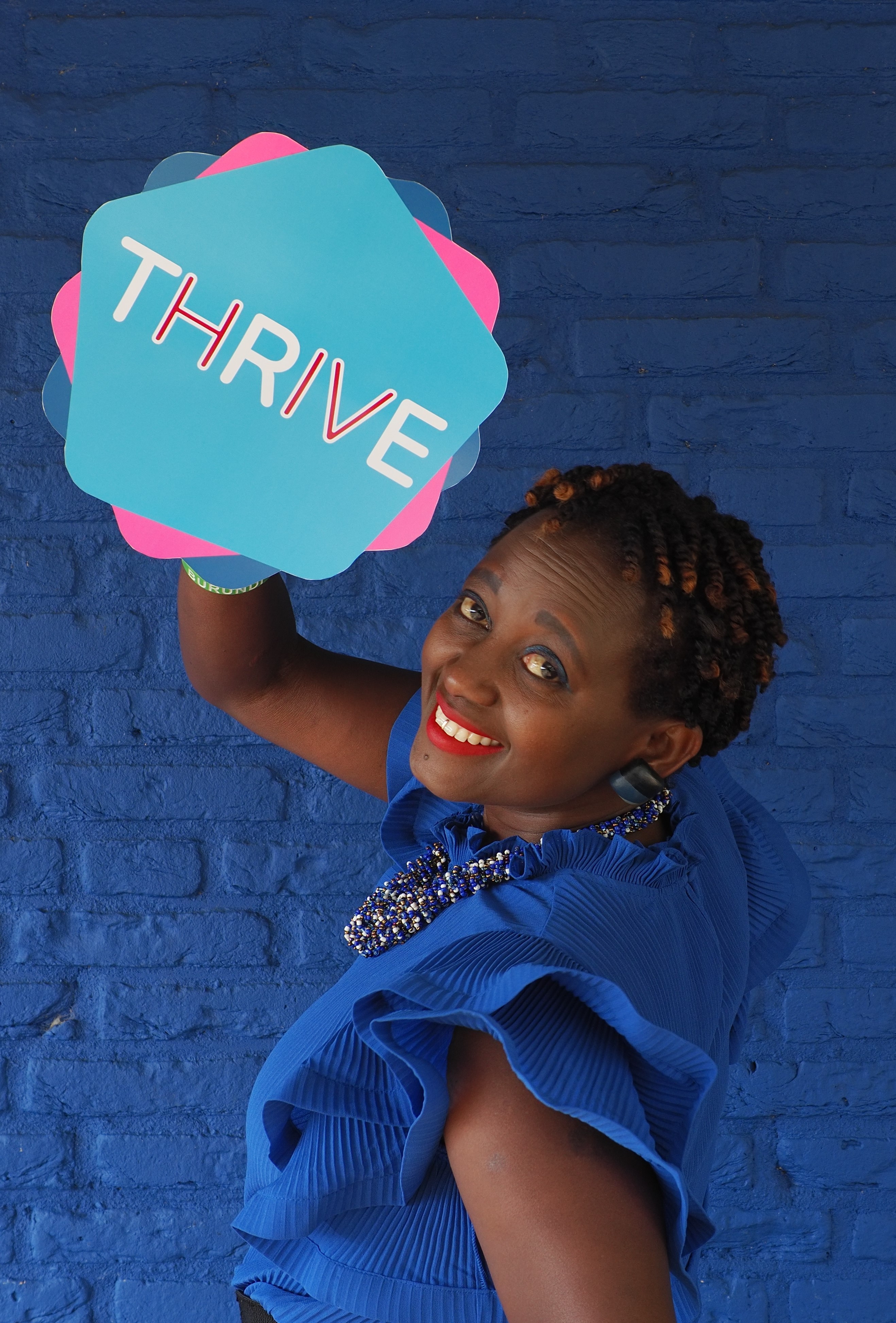 Eliane (HIVstigmafighter) holding a sign that reads &quot;THRIVE&quot;.