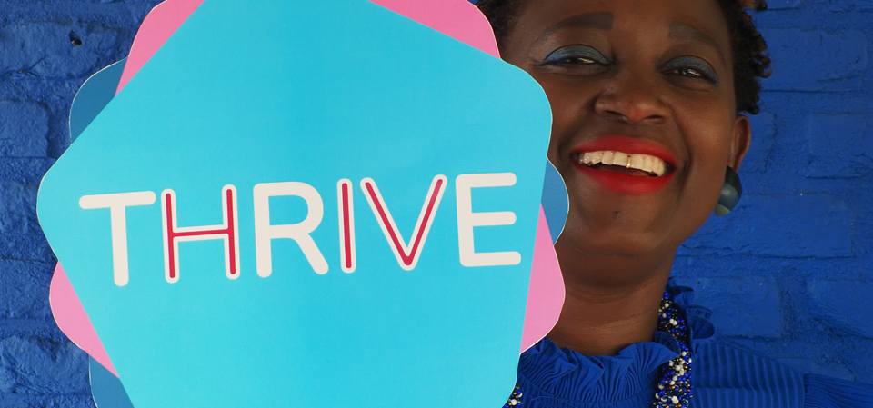 Eliane (HIVstigmafighter) holding a sign that reads &quot;THRIVE&quot;.