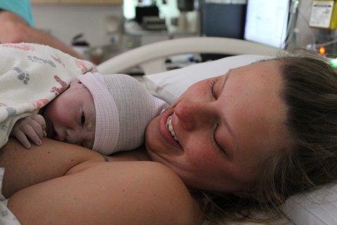 Heather O'Connor in hospital bed, smiling, holding newborn baby on her chest.