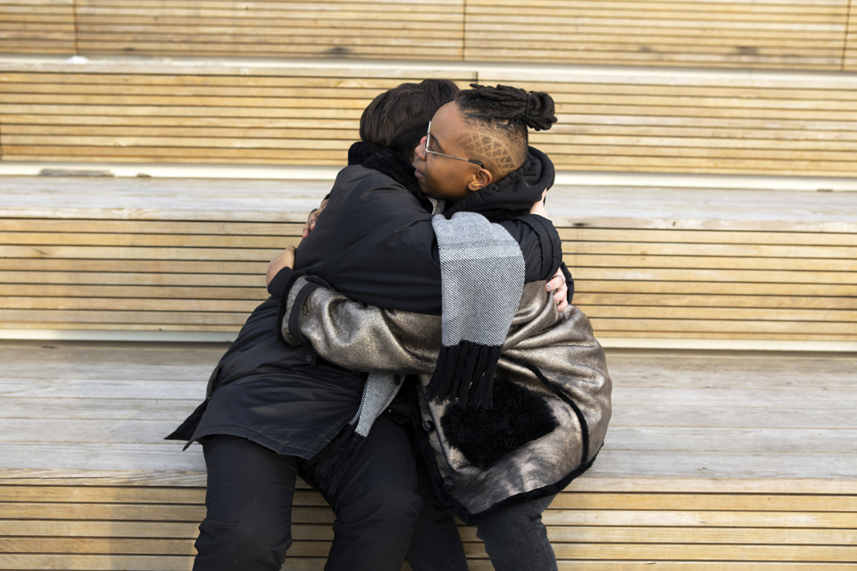 Two people sitting next to each other, hugging.