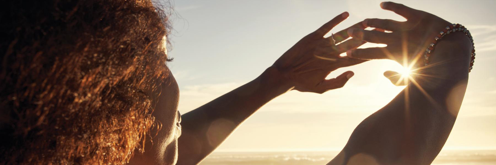 Woman looking through her hands towards the sun.