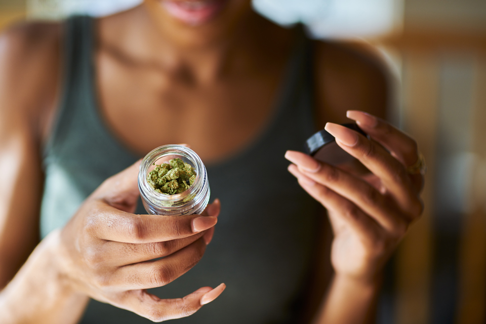 Mujer abriendo un frasco de marihuana (cannabis/hierba) legal.