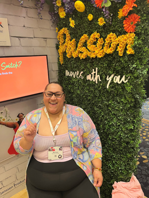 Marissa Gonzalez at USCHA 2023 in front of a floral sign that reads &quot;Passion moves with you&quot;.