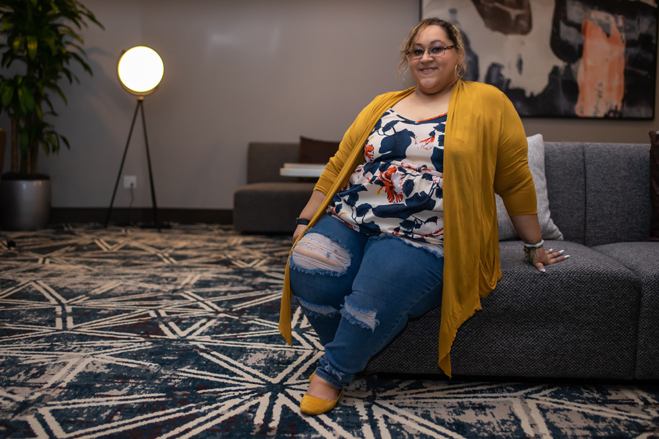 Marissa Gonzalez, sitting on a sofa, smiling.