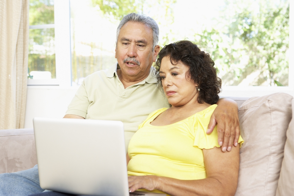 Una pareja mayor sentada en un sofá mirando una laptop juntos.