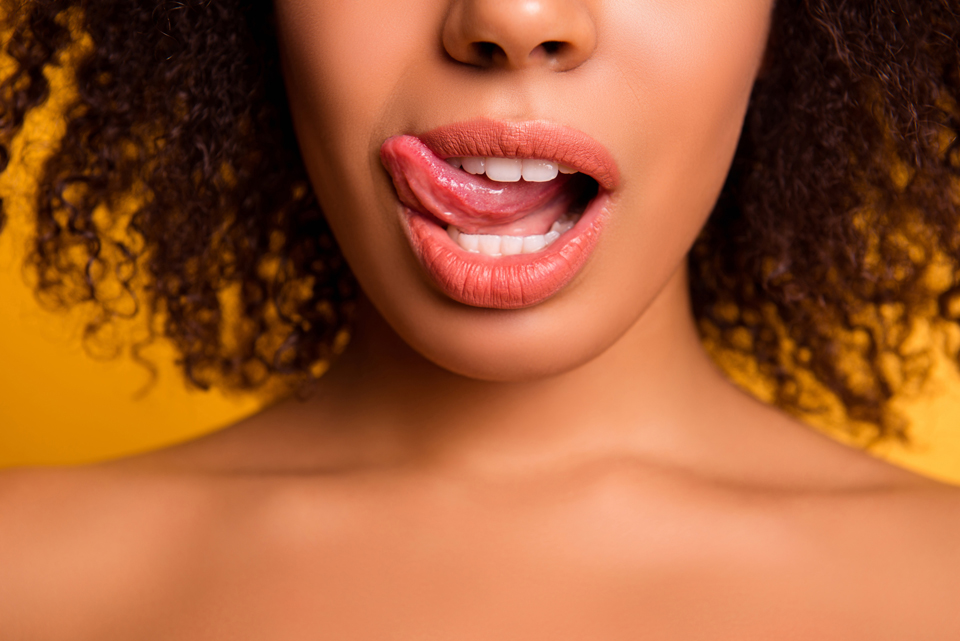 Close up of woman from bottom of nose to top of chest, her tongue licking her upper lip.