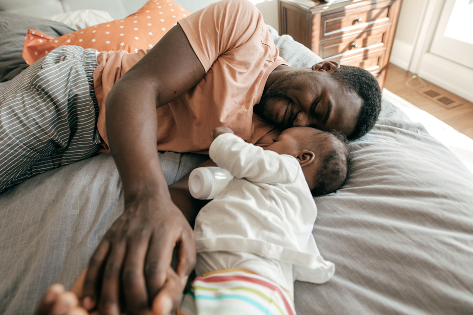 Padre y bebé con biberón en una cama.