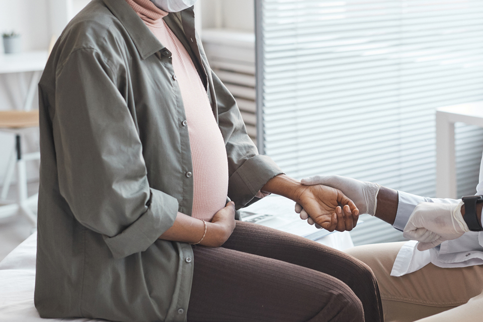 Pregnant person sitting on examination table getting pulse taken. 