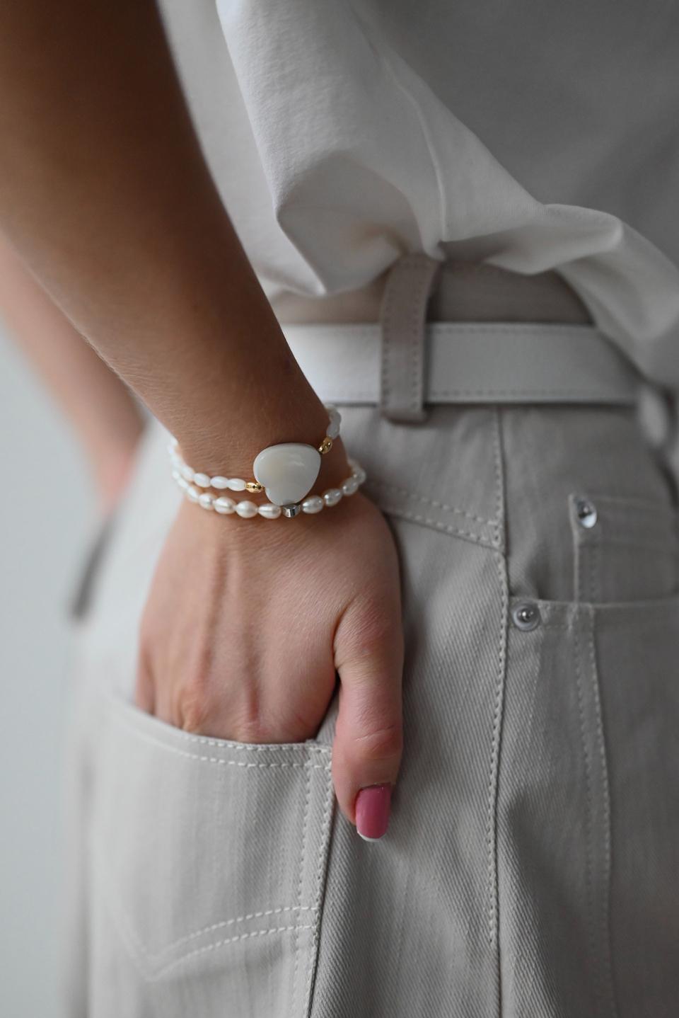 Hand with heart bracelet in back pocket of pants.