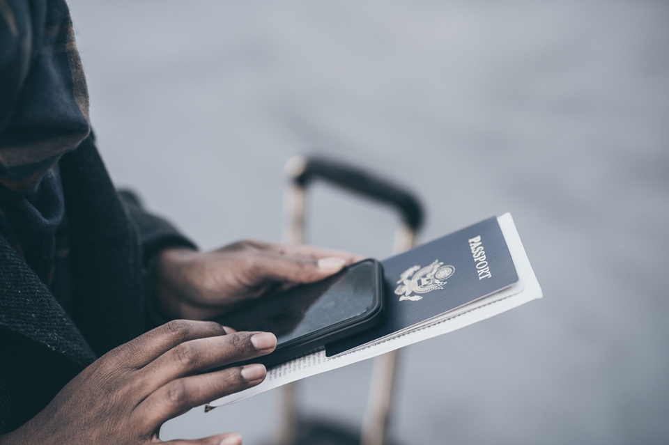 Hands holding a passport with luggage nearby.