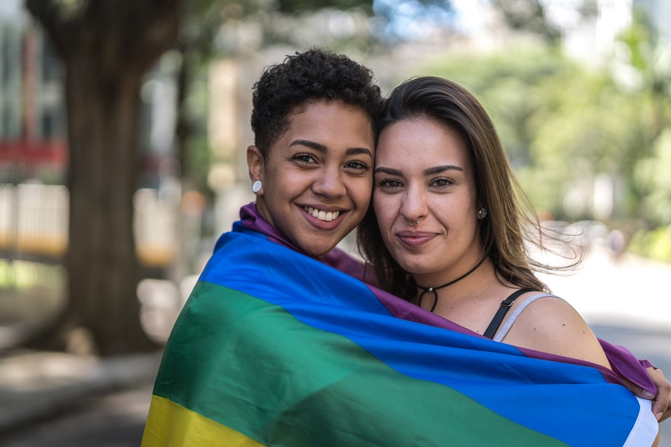 Two people smiling and hugging, wrapped in colorful flag.