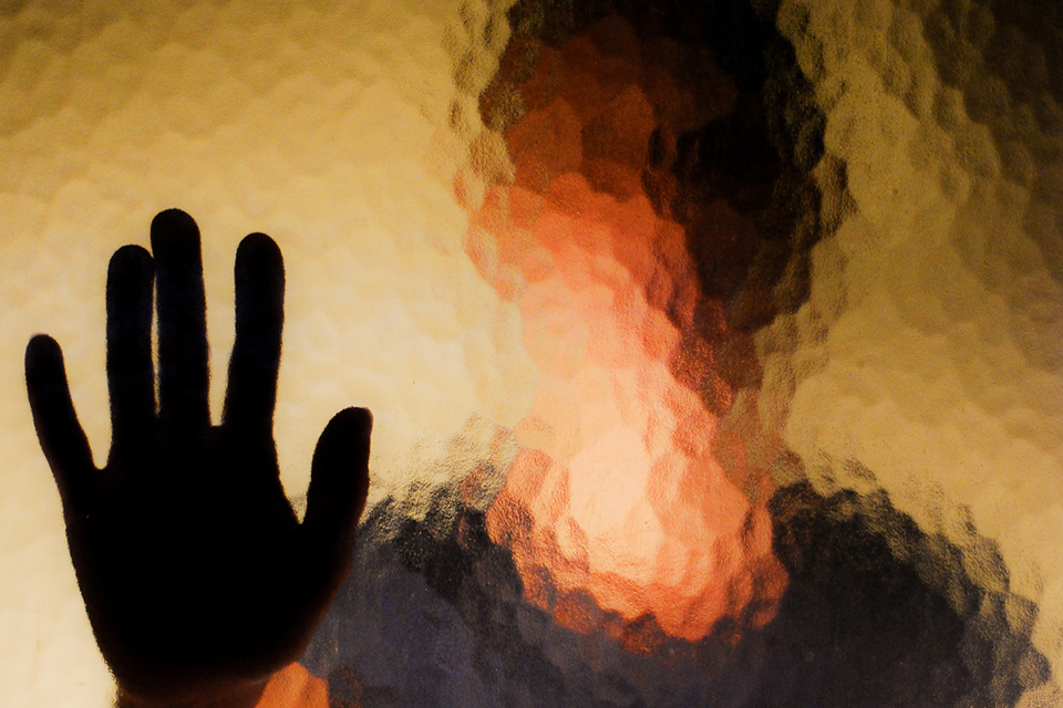 Blurry face of woman with hand against glass.