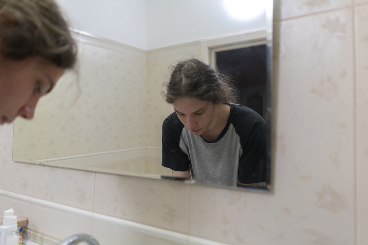 Person at bathroom sink with mirror in front of them.