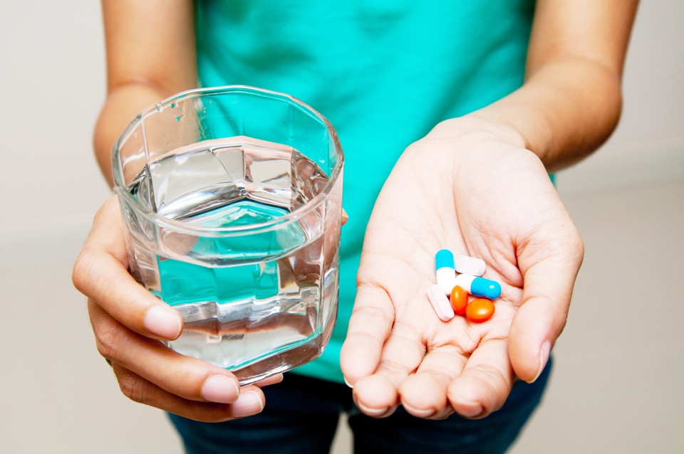 Person's hands holding pills in one and a glass of water in the other.