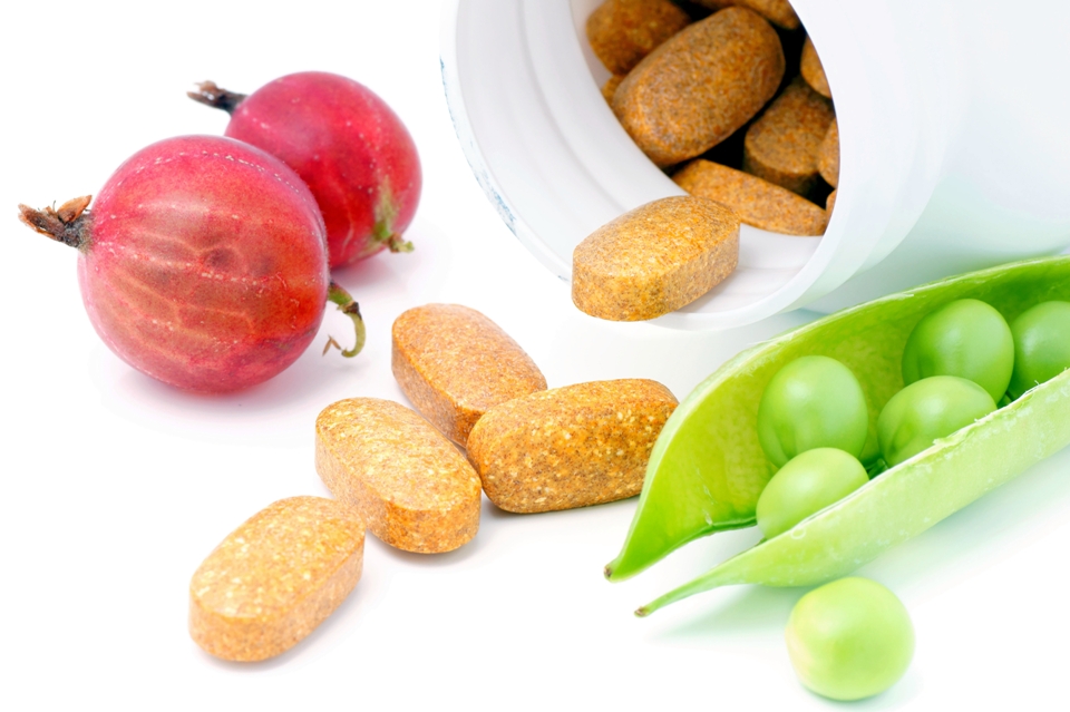 Vitamins spilling out of a bottle and vegetables.