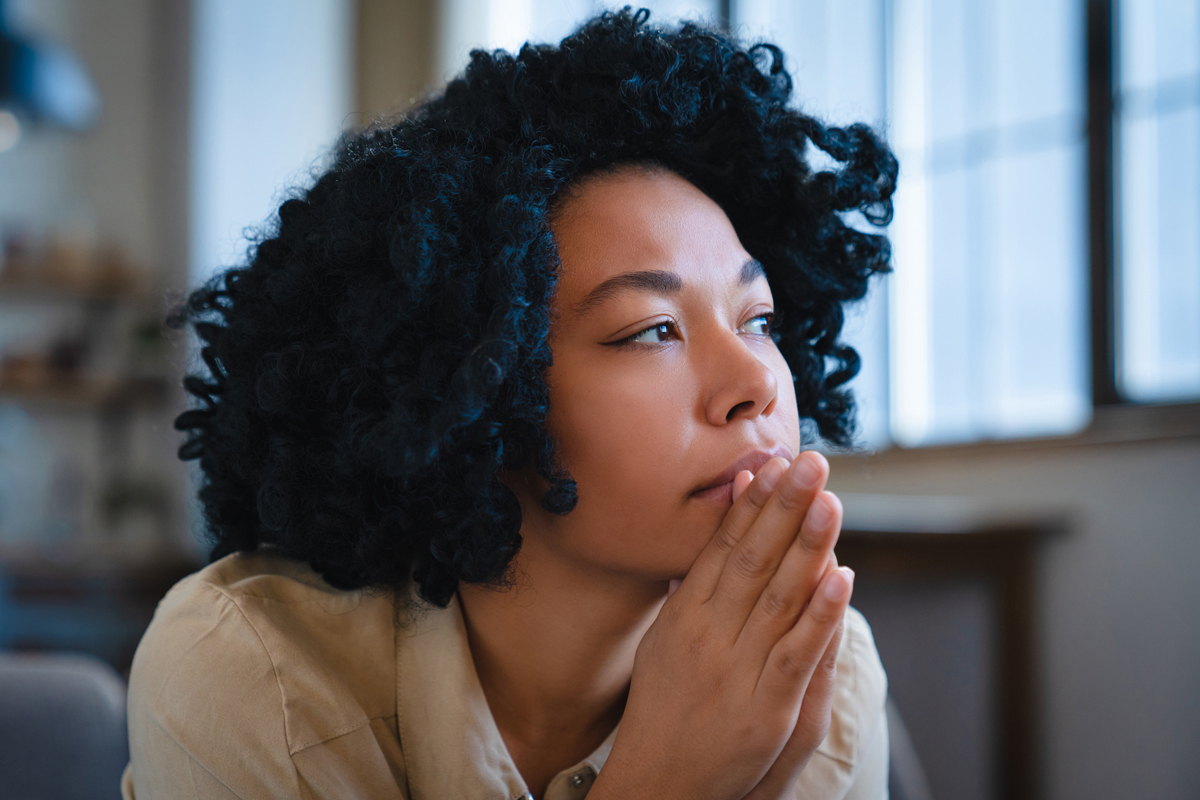Woman with hands together in front of chin looking up and to the side.