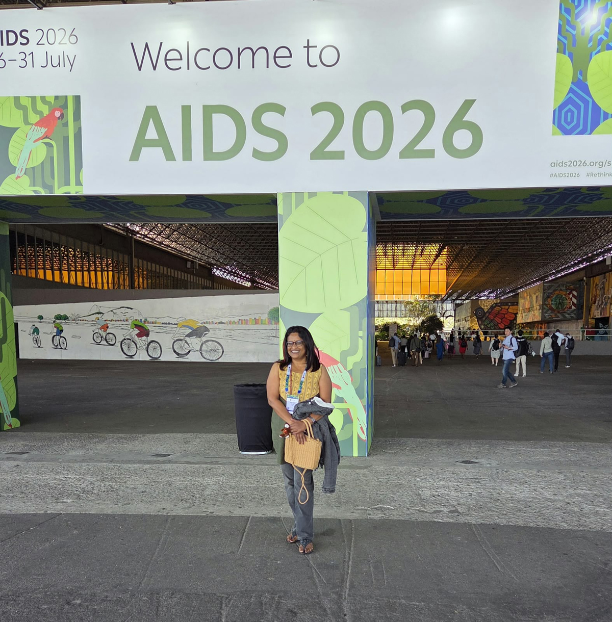 The Well Project global ambassador Jyoti Dhawale in front of sign that reads "Welcome to AIDS 2026".