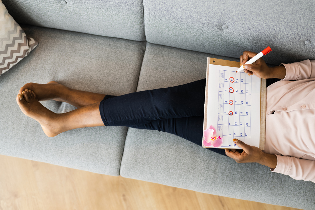 Woman on sofa circling dates on calendar.