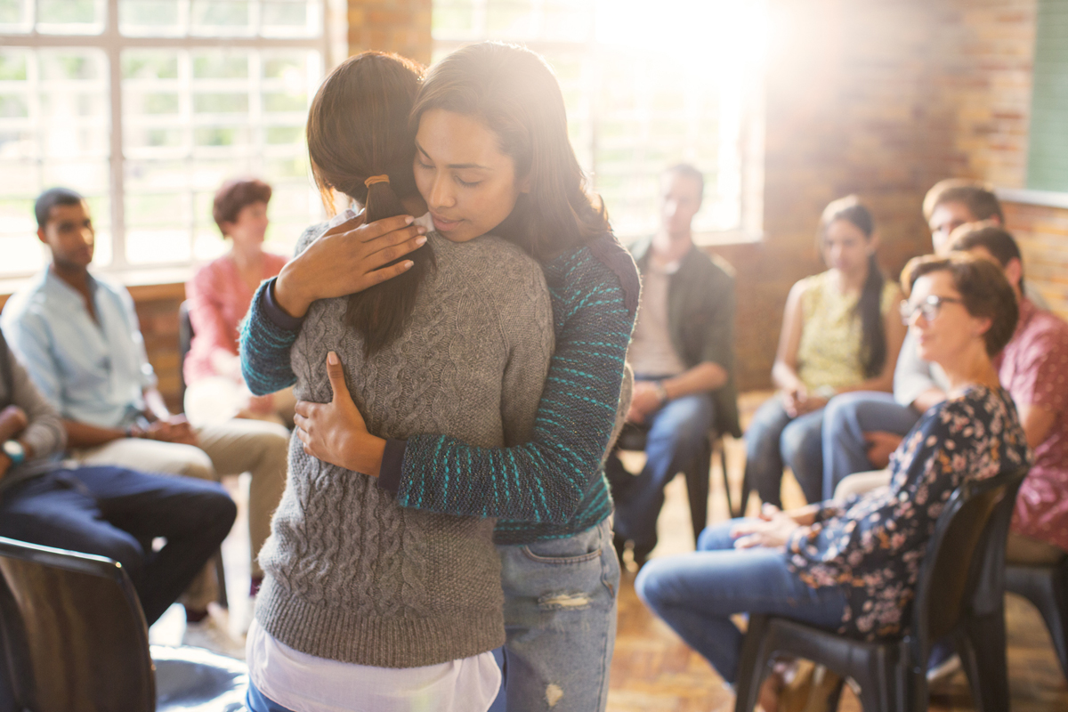 Two women hugging in group therapy session.