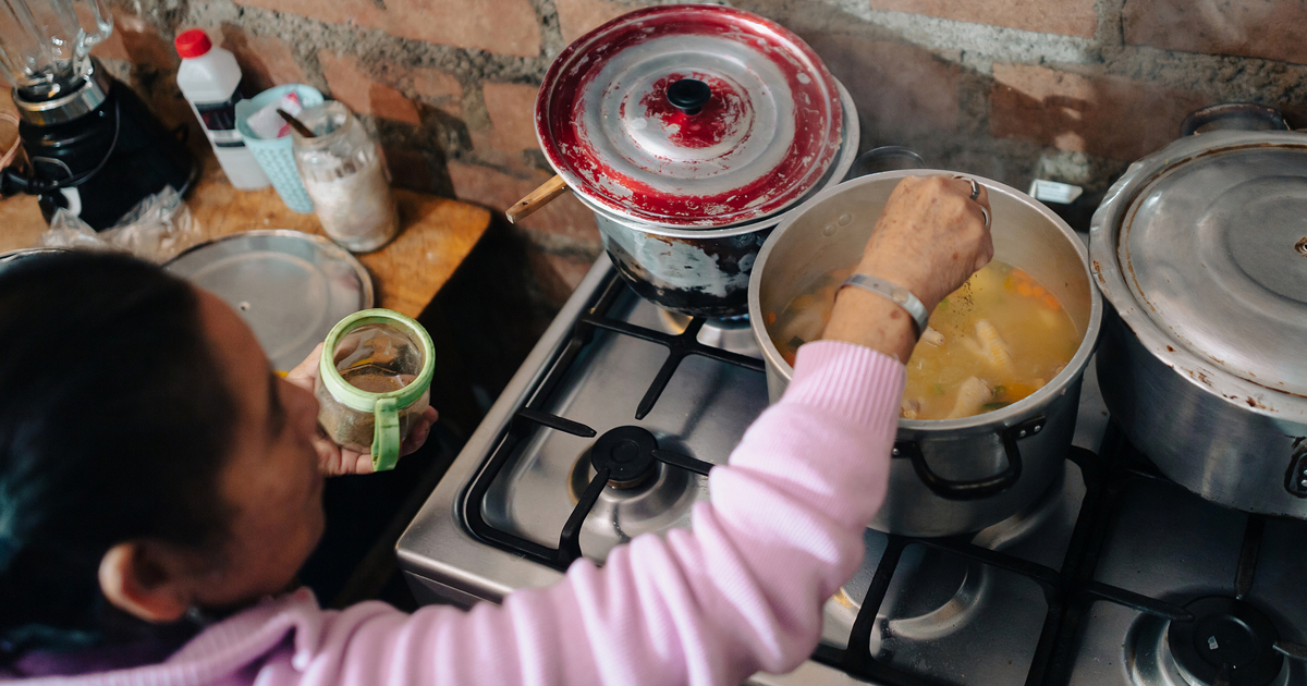 Woman in a kitchen, cookng at a stove.