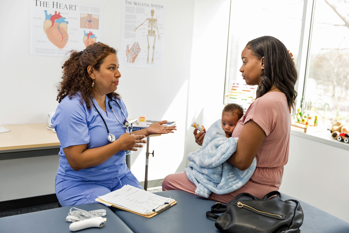 Woman holding baby talking to doctor in medical office.