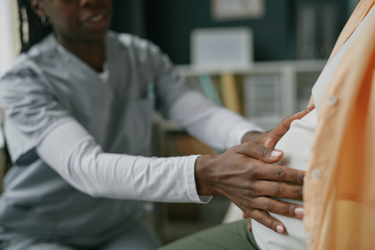 Healthcare professional examining pregnant person, hands touching abdomen.