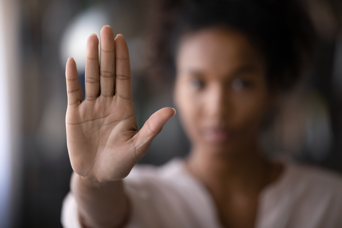 Woman with blurred face holding one hand in front of her, palm forward.