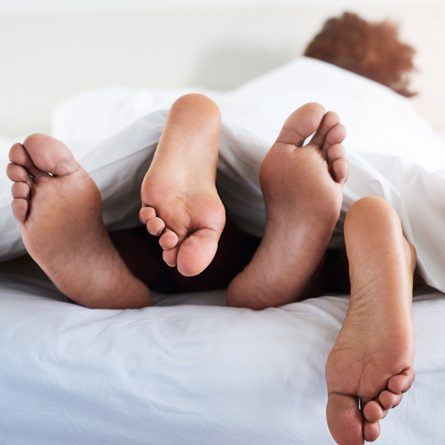 Los pies de dos personas asomando por debajo de las sábanas