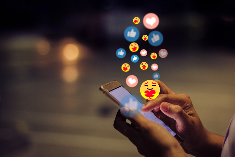 Woman using a smartphone on social media with emoji reactions floating out of phone.