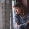 Mujer sentada mirando por la ventana cruzando los brazos alrededor de sí misma.