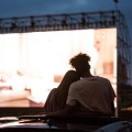 Silueta de la espalda de dos personas sentadas con los brazos alrededor de la otra, viendo una película al aire libre.