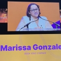 Marissa Gonzalez on a stage with screens behind her showing her - and an audience in front.