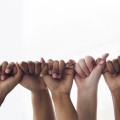 Hands of various skin tones linking pinky to thumb in a row.