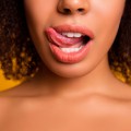 Close up of woman from bottom of nose to top of chest, her tongue licking her upper lip.