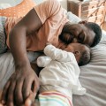 Parent and baby with a bottle on a bed.