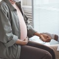 Pregnant woman sitting on examination table getting pulse taken. 