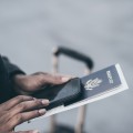 Hands holding a passport with luggage nearby.
