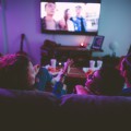 Three teens sitting down, talking and watching TV together at home.