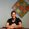 Gina Brown, RSW, smiling, sitting with arms crossed at table in front of wall art.
