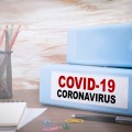 Pencil cup, pencils, notepad, and two binders on desk. One binder is labeled "COVID-19 Coronavirus".