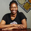 Gina Brown, RSW, smiling, sitting with arms crossed at table in front of wall art.