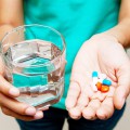 Person's hands holding pills in one and a glass of water in the other.