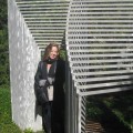 Vickie Lynn, smiling, standing outside in front of abstract metal sculpture in garden.