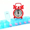 Weekly pill organizer with pills inside some sections and an alarm clock on top.