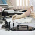 Gloved hands holding test tubes and using lab equipment.