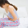 Profile of woman sitting on the side of a bed holding her stomach.
