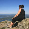 Back profile of woman sitting on rock looking at sea. 