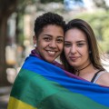 Two people smiling and hugging, wrapped in colorful flag.