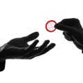 Silhouette of hand giving another hand a condom.