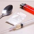Spoon, clear bag of white powder, syringe with liquid inside it, and red lighter on a counter.